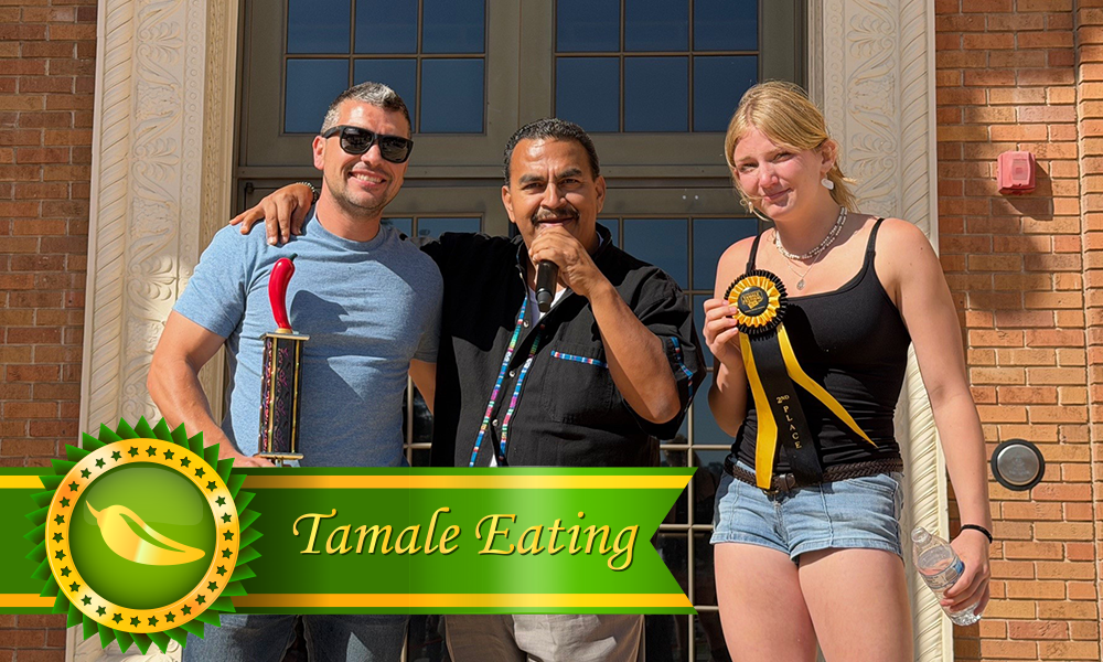 Group photo of the 2026 Tamale Festival Tamale Eating Contest winners (age 12+), with one person holding a trophy and another holding a ribbon, standing on either side of the event MC.
